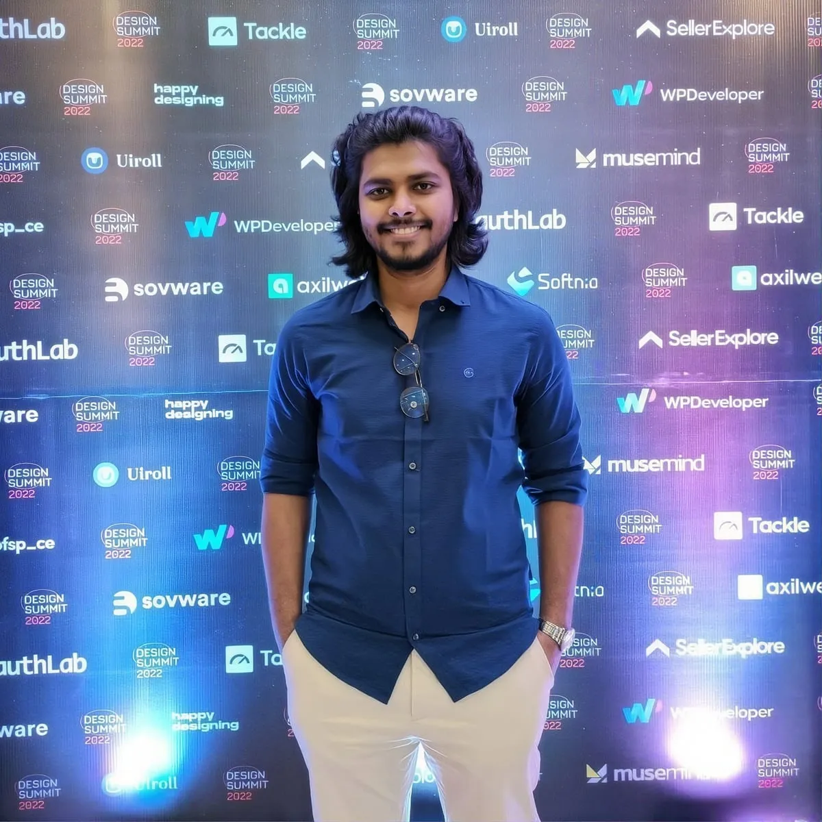Masum Rana smiling, standing in front of a Design Summit 2022 sponsor wall